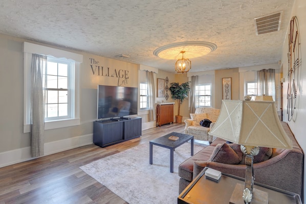 A living room with a TV, sofa, coffee table, and a sign that reads 'The Village Loft'.