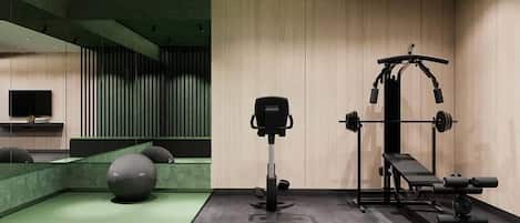 A gym with exercise equipment, a TV, and a green cushioned area.