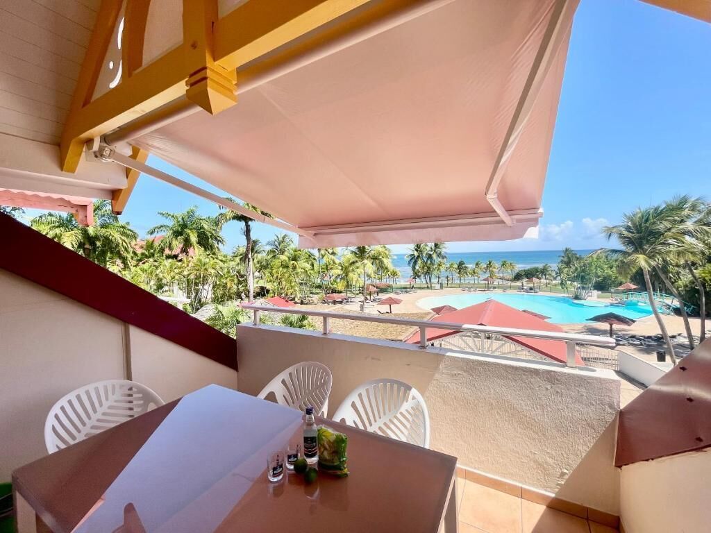 A balcony with a table, chairs, and a view of a pool and beach.