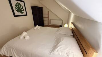 A neatly made bed with white linens and towels, a framed leaf artwork on the wall, and a wooden headboard.