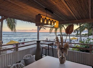 A beachside restaurant with a view of the ocean, a thatched roof, and outdoor seating. - Sur la Plage - Club Sainte-Anne (Sainte-Anne)