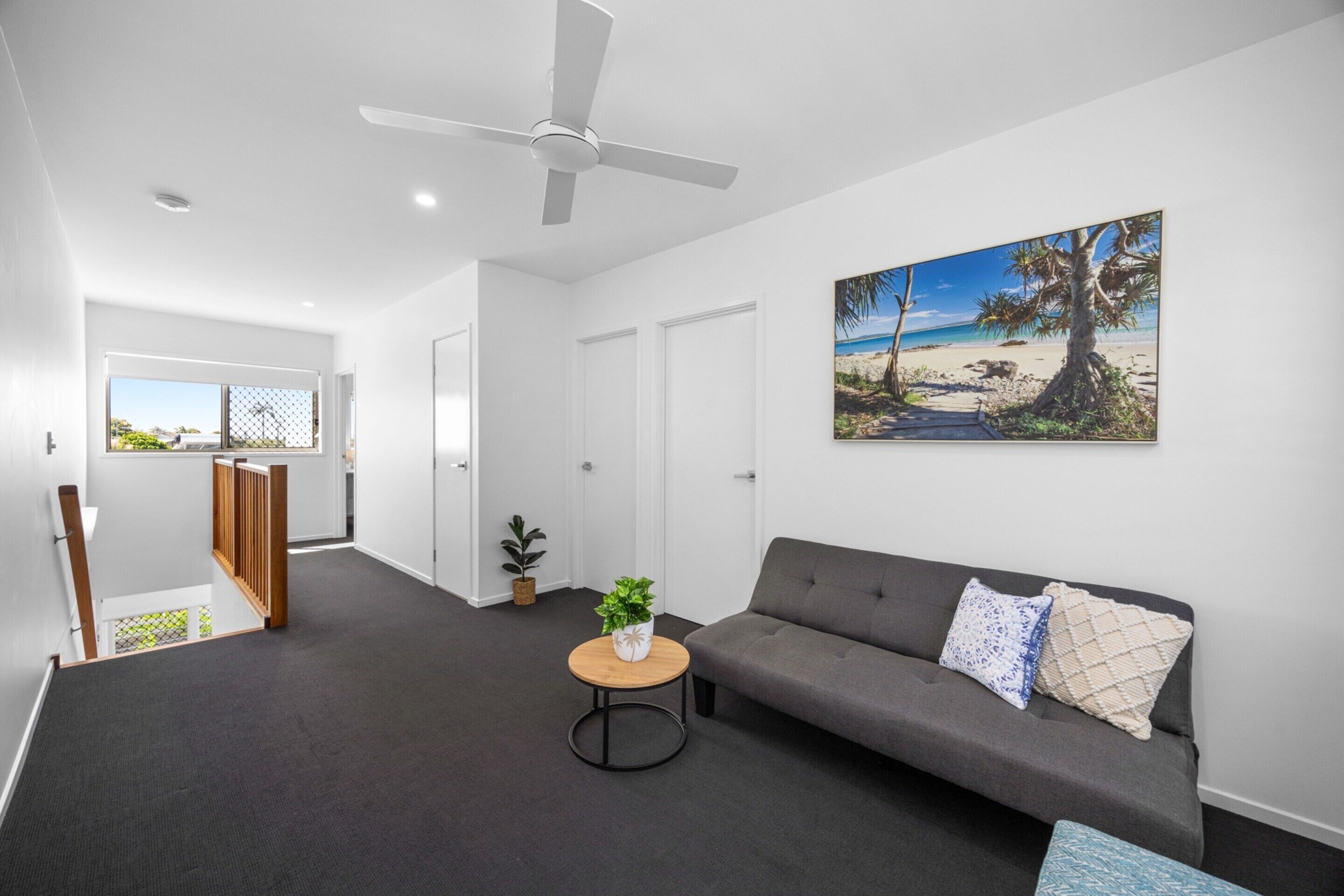 A modern living room with a grey sofa, a round coffee table, and a ceiling fan.
