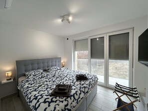 Ein Schlafzimmer mit einem großen Bett, einem Fenster mit Jalousien, einer Deckenleuchte und einem Sessel.