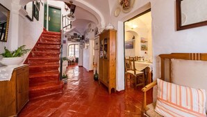 Un pasillo con una escalera de madera, una zona de comedor con una mesa y sillas, y un sofá.