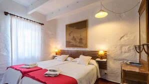 Un dormitorio con dos camas, un cuadro en la pared, una lámpara y una silla de madera.
