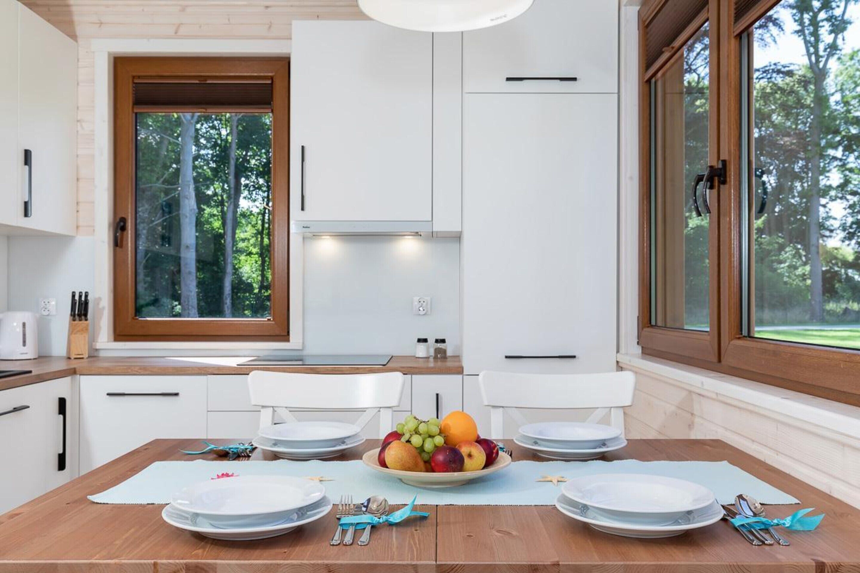 A modern kitchen with white cabinets, a wooden countertop, and a dining area with a table set for two.