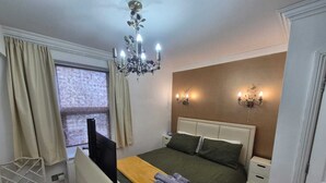 Habitación de hotel con cama, mesitas de noche, escritorio con silla, televisor, candelabro y dos apliques de pared.