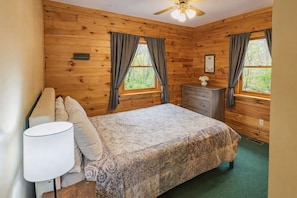 Ein Zimmer mit Holzwandverkleidung, einem Bett, einem Schminktisch und einem Nachttisch.