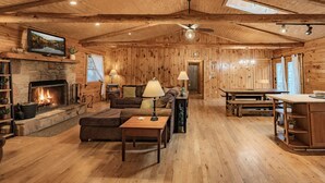 A log cabin interior with a fireplace, wooden furniture, and a dining area.