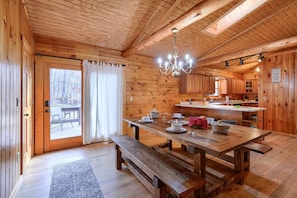 Ein rustikales Holzhaus-Interieur mit Esstisch, Bänken, einer Kronleuchter und einer Küchenzeile.