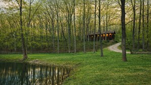 A cabin in a wooded area with a pond and a dirt path leading to it.
