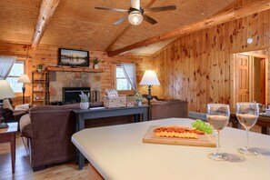Ein Holzinnenraum mit Kamin, Sofas, einem Esstisch mit Snacks und Weingläsern.