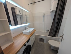 A modern bathroom with a built-in washing machine, a bathtub, a toilet, and a large mirror. - Great Apartment in Tieschen 4 People and A-C (Tieschen)