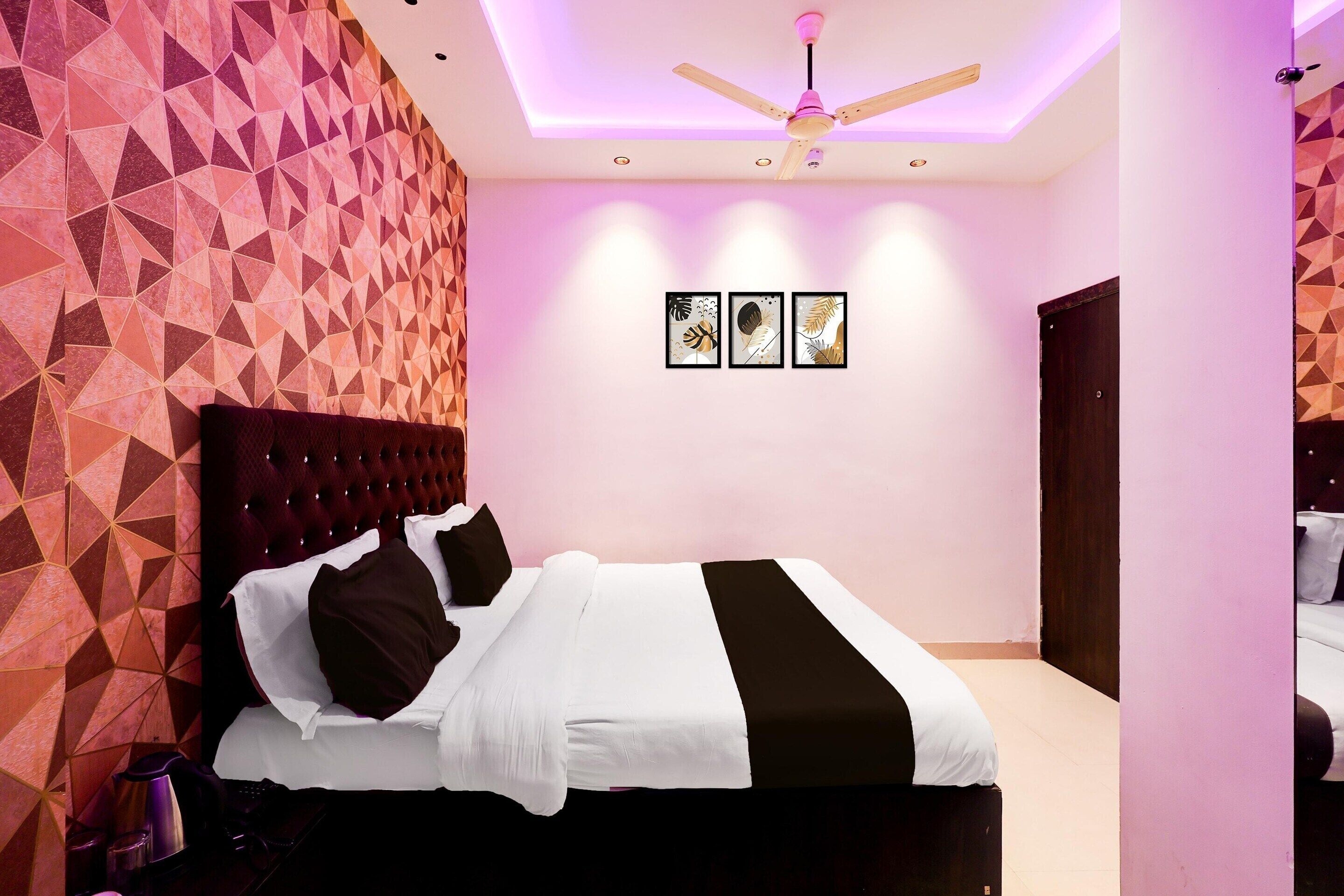 A modern bedroom with a geometric-patterned wall, a tufted headboard, a ceiling fan, and three framed artworks on the wall.