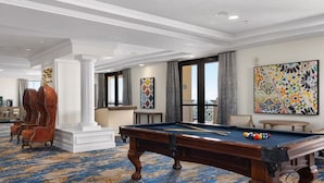 Une table de billard dans une pièce dotée d’un tapis à motifs, d’un grand tableau abstrait et d’une vue par la fenêtre.