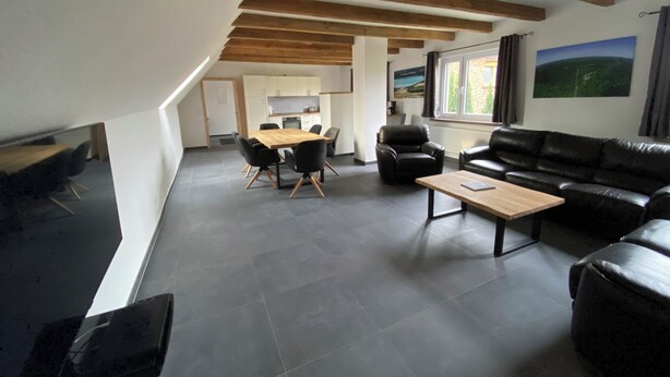 Een moderne woonkamer met een eethoek, een bank, een salontafel en een keuken op de achtergrond.