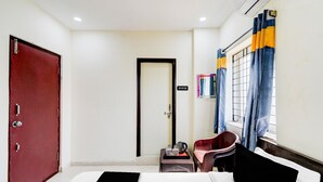 Una habitación de hotel con cama, un escritorio y una silla, una puerta roja y una ventana con cortinas.