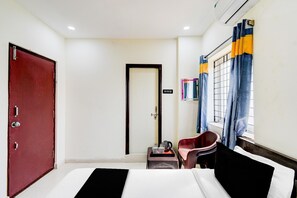 Habitació d'hotel amb un llit, escriptori amb cadira, una porta vermella i una finestra amb cortines.