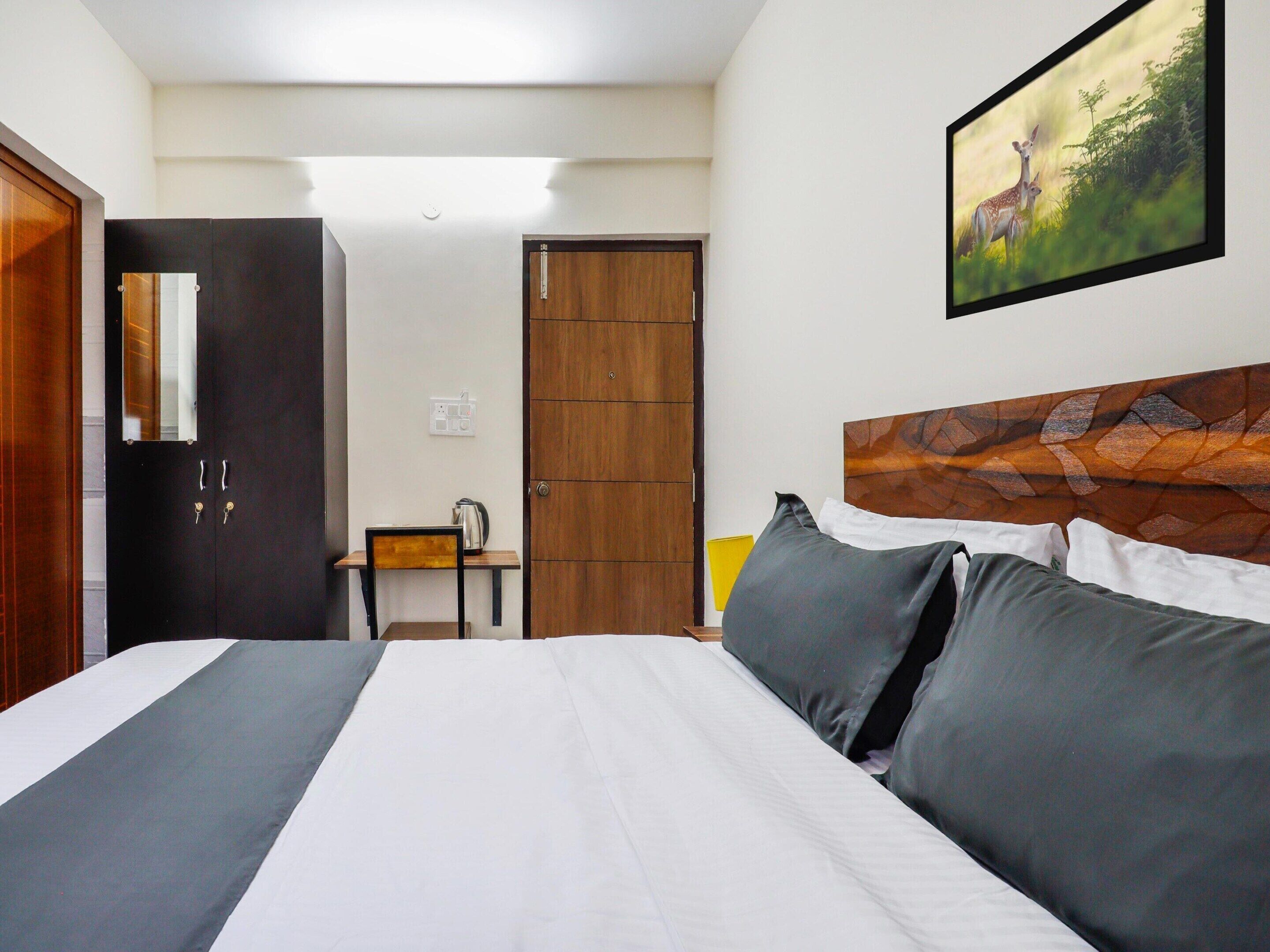 Ein Hotelzimmer mit einem Bett, einem Schreibtisch, einem Stuhl, einem Holzschrank, einem Spiegel und einem Bild an der Wand.