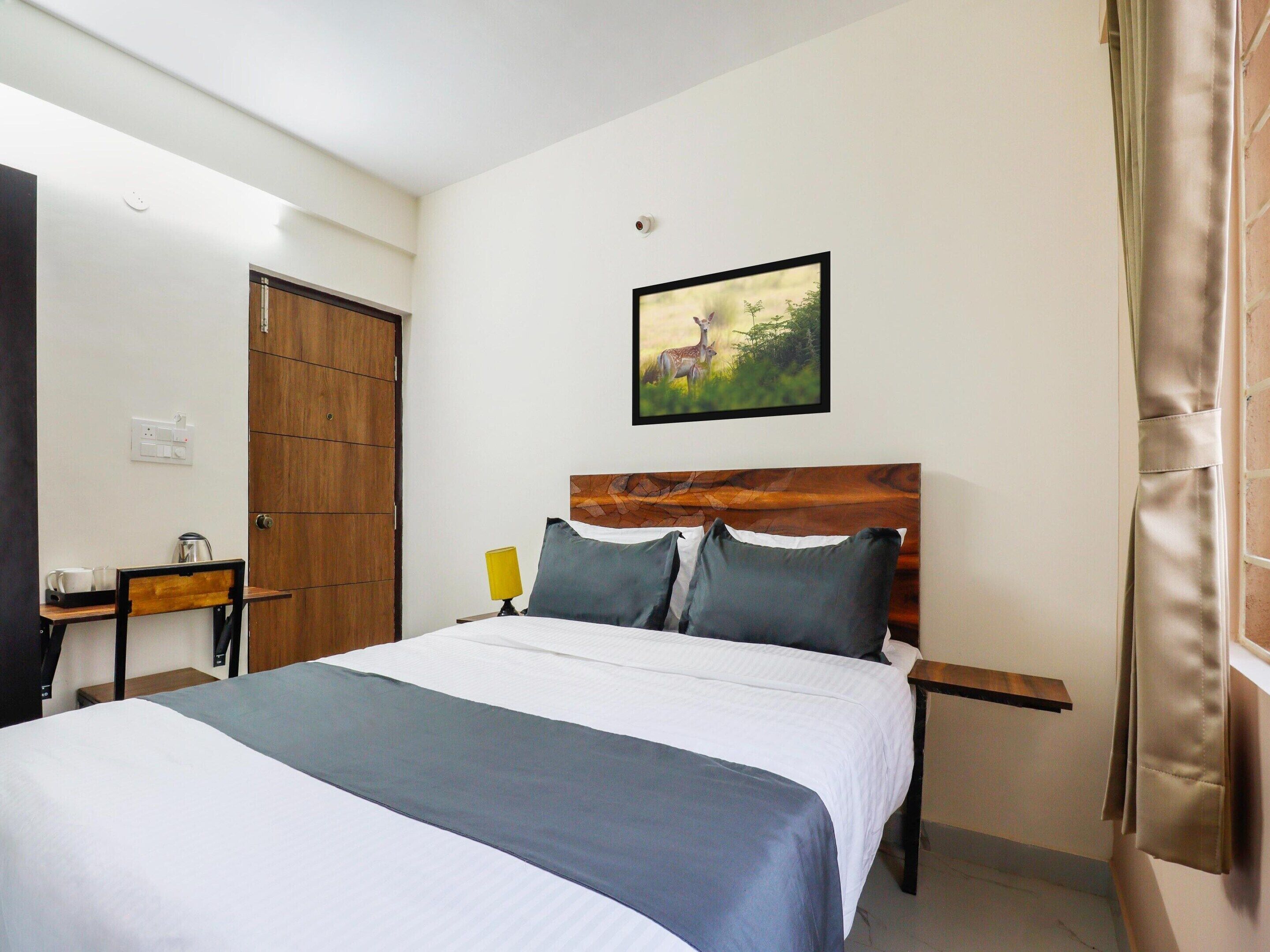 A hotel room with a bed, a desk, a chair, a lamp, and a painting on the wall.