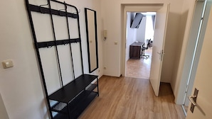 A hallway with a black metal rack, a wooden floor, and a door leading to a room with a desk and chair. - Nice Apartment in the Center of Klöch (Kloech)