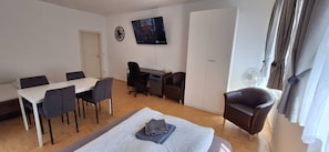 Ein Zimmer mit Bett, Schreibtisch, Stuhl, Esstisch und Fernseher.