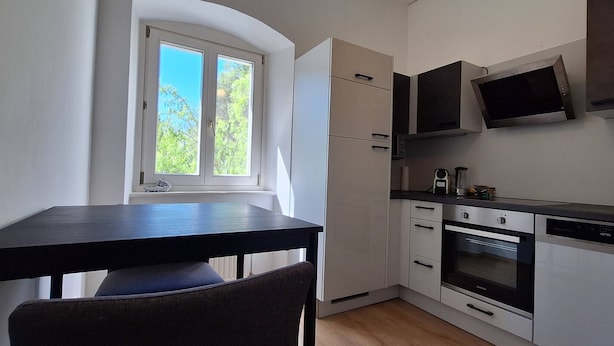 A compact kitchen with white cabinets, a black countertop, and a window with a view of trees. - Nice Apartment in the Center of Klöch (Kloech)