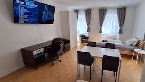 A compact hotel room with a bed, a desk, a chair, a TV, and a window with curtains. - Nice Apartment in the Center of Klöch (Kloech)