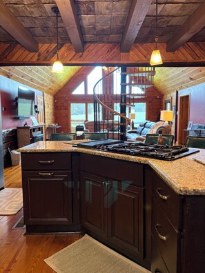 Una cocina con gabinetes de madera oscura, encimeras de granito, una isla central y una escalera de caracol que lleva a un altillo.