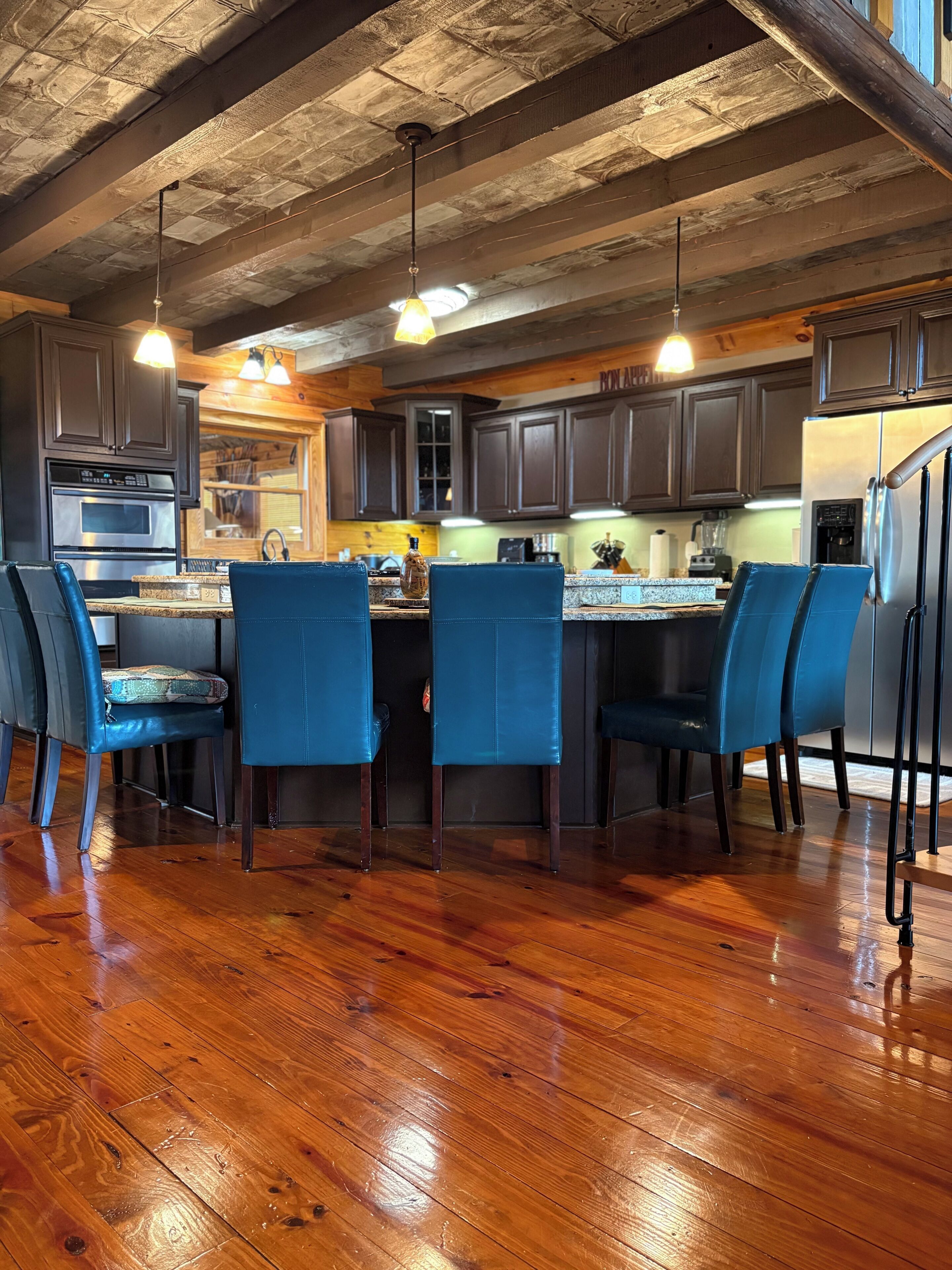 A kitchen with wooden floors, dark cabinets, and blue chairs.