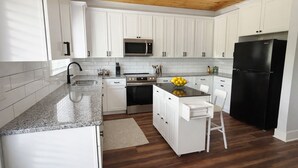 Una cocina moderna con armarios blancos, un refrigerador negro, un microondas y un lavamanos.