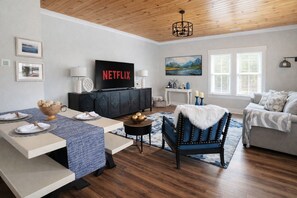 Una sala de estar con techo de madera, televisor, sofá, mesa de comedor y un cuadro en la pared.