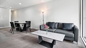 Una sala de estar moderna con un sofá gris, una mesa de comedor con sillas, una mesa de centro de mármol y un jarrón con flores.
