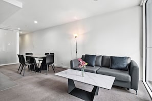 Een moderne woonkamer met een grijze bank, een eettafel met stoelen, een marmeren bijzettafeltje en een vaas met bloemen.