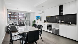 Una cocina moderna con gabinetes blancos, un protector contra salpicaduras negro y electrodomésticos de acero inoxidable.