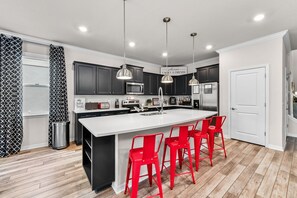 A modern kitchen with a large island, dark cabinets, stainless steel appliances, and red bar stools. - Mickey, Pooh & Jurassic Rooms • Theater • Arcade & Pinball • Pool & Spa • 2166 (Davenport)