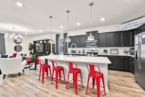 A modern kitchen with a central island, bar stools, and a 'welcome family & friends' sign. - New Listing! Classic Mickey! Theater! Resort 7 mi 2 Disney! 2166 (Davenport)