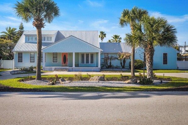 A light blue house with a red door, surrounded by palm trees and a well-maintained lawn. - Paradise Spaces Resort (St. Augustine)