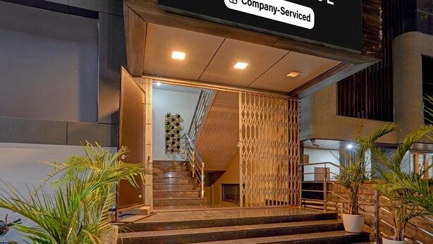 Entrada de un hotel con escaleras, plantas en macetas y un letrero que dice 'Company-Serviced'.