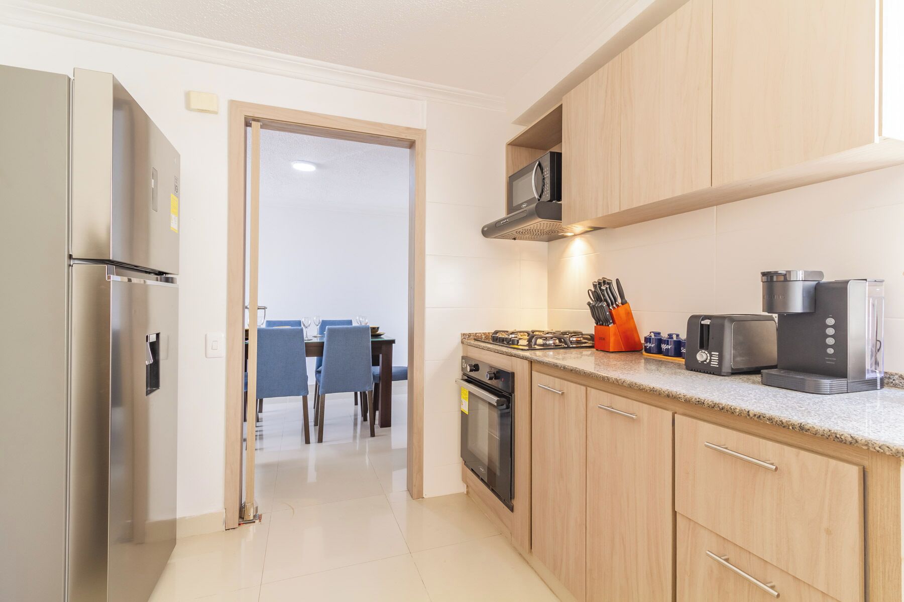 Een moderne keuken met roestvrijstalen apparatuur, houten keukenkastjes en een eethoek met blauwe stoelen.