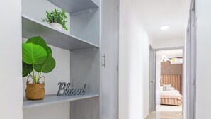 A hallway with a grey wardrobe, a shelf with a plant and a 'Blessed' sign, and a glimpse of a bedroom with a bed and a ceiling fan. - Altos del parque By Host Pro (Barranquilla)