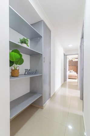 A hallway with a grey wardrobe, a shelf with a plant and a 'Blessed' sign, and a glimpse of a bedroom with a bed and a ceiling fan. - Altos del parque By Host Pro (Barranquilla)