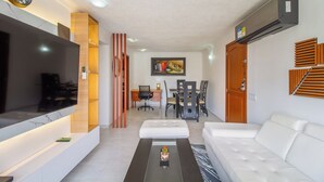 A modern living room with a flat-screen TV, a sofa, a coffee table, and a dining area with chairs and a table. - Altos del parque By Host Pro (Barranquilla)