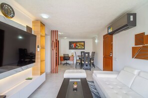 A modern living room with a flat-screen TV, a sofa, a coffee table, and a dining area with chairs and a table. - Altos del parque By Host Pro (Barranquilla)