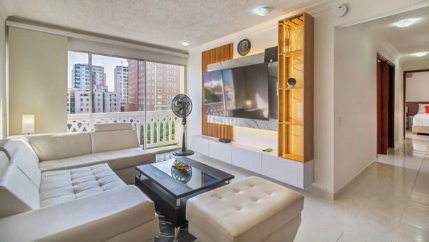 A modern living room with a sofa, a glass coffee table, a TV, and a fan. - Altos del parque By Host Pro (Barranquilla)