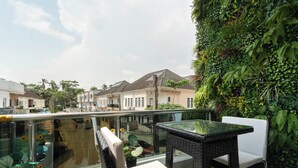 A balcony with a glass railing, wicker furniture, and a lush green wall.