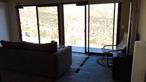 Un salon comprenant un canapé, un fauteuil et une table. De grandes portes-fenêtres coulissantes donnent sur un balcon d’où l’on peut admirer un paysage désertique.