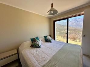 A bedroom with a large bed, a view of mountains through a window, and a hanging light fixture. - Gorgeous 3-bedroom farmhouse in charming San Esteban awaits you (San Esteban)