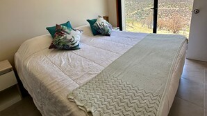 Une chambre avec un grand lit, une vue sur les montagnes par la fenêtre et un luminaire suspendu.