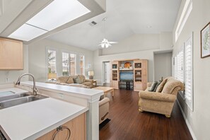 A modern kitchen with a central island, a dining area with a sofa and table, and a living room with a couch and a TV. - Loma Vista Escape - 4BR Pool Home Near Disney, Golf & Shopping (Davenport)